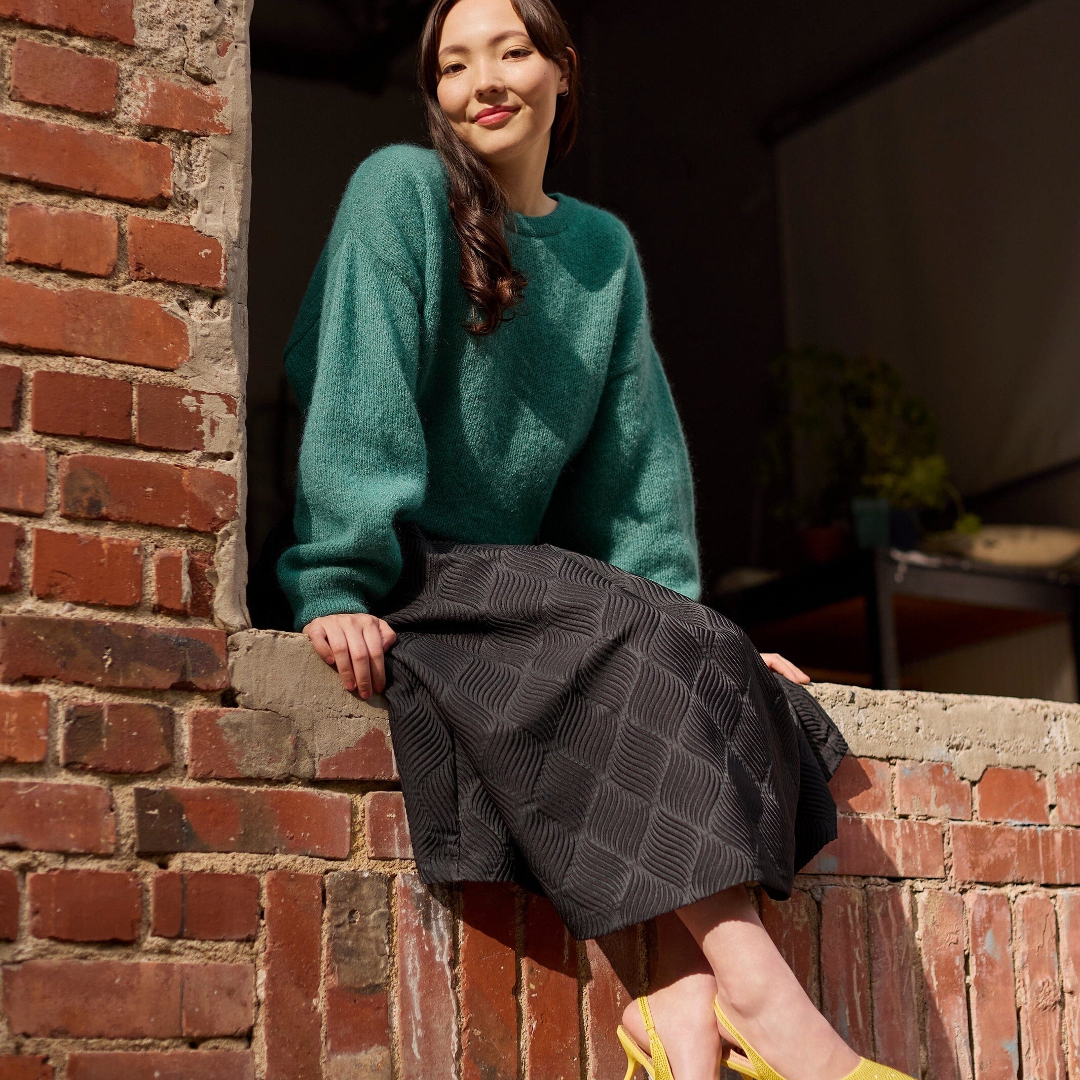 nainen istuu ulkona yllään naisten midimittainen musta jacquard-hame vyötärön laskoksilla ja vetoketjukiinnityksellä, yhdistettynä Mohair sweater neulepaitaan värissä wasabi.