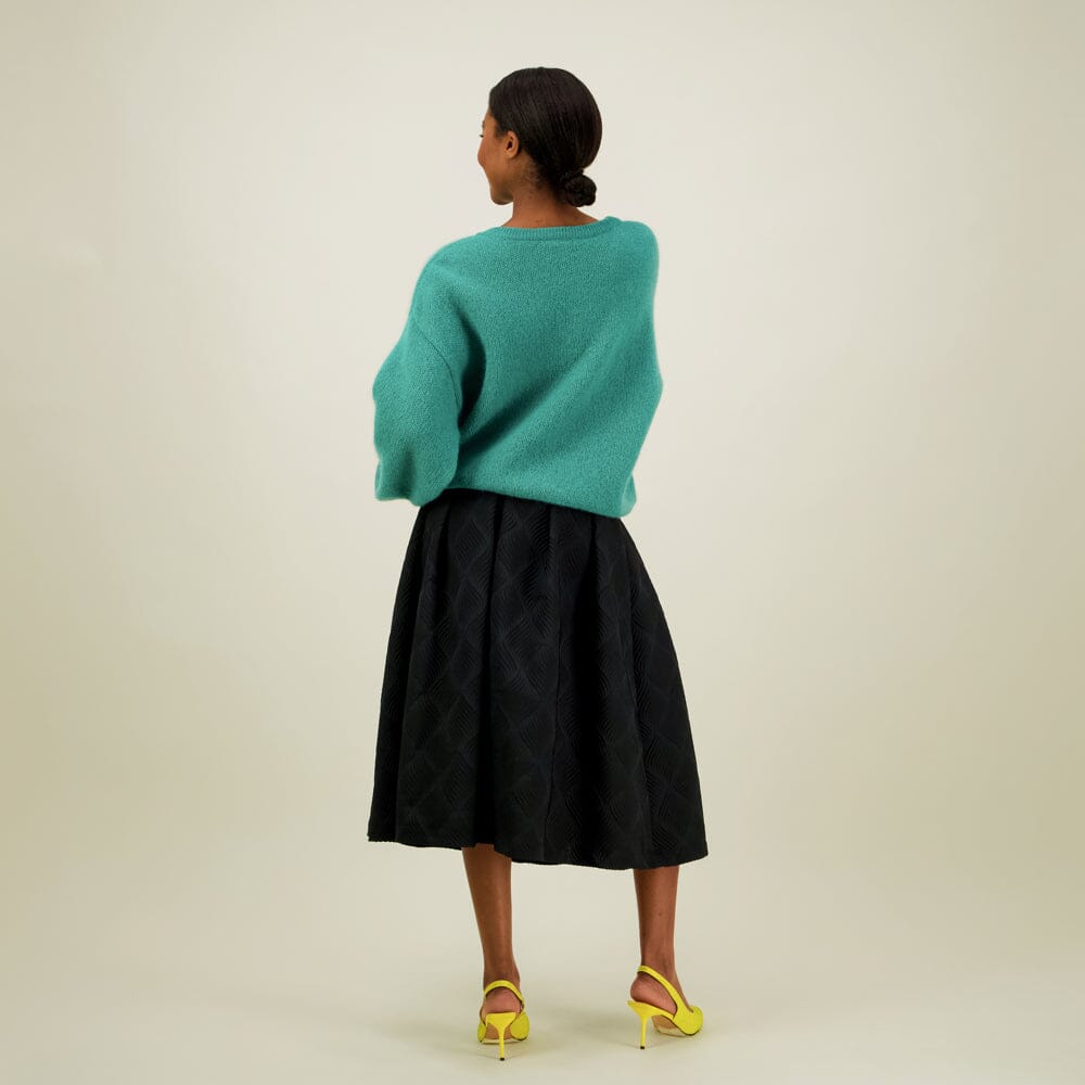 Naisten midimittainen musta jacquard-hame vyötärön laskoksilla ja vetoketjukiinnityksellä, yhdistettynä Mohair sweater neulepaitaan värissä wasabi, kuva takaa päin.
