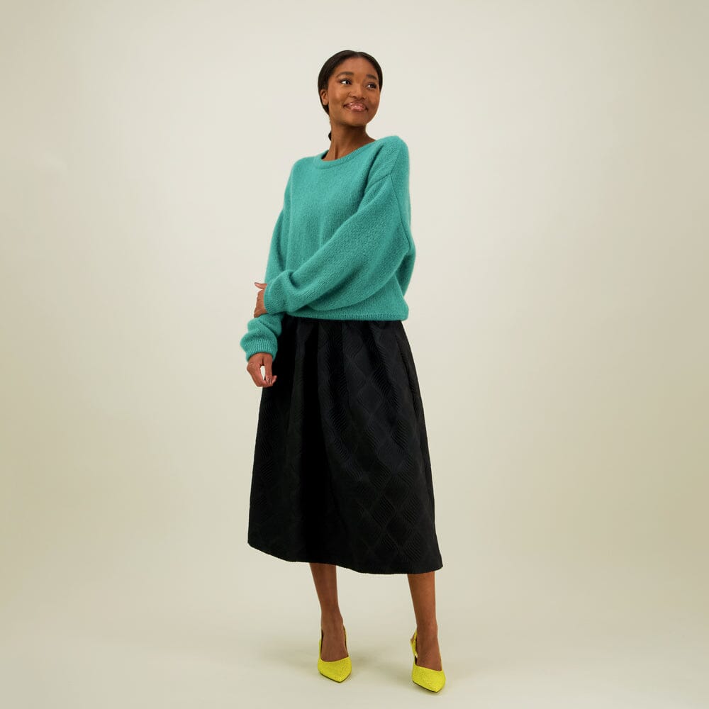 Naisten midimittainen musta jacquard-hame vyötärön laskoksilla ja vetoketjukiinnityksellä, yhdistettynä Mohair sweater neulepaitaan värissä wasabi. 